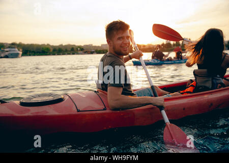 Certain young caucasian couple kayak sur rivière avec coucher du soleil dans l'arrière-plan. Avoir du plaisir dans l'activité de loisirs. Romantique et heureux homme et femme sur le kayak. Le sport, les relations concept. Banque D'Images