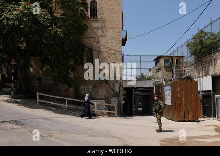 Un soldat israélien garde tandis que la femme palestinienne traverse Bab El-Zawiya en traversant le quartier palestinien de Bab a-Zawiya et la zone de contrôle israélienne H-2 dans la ville divisée d'Hébron en Cisjordanie Banque D'Images