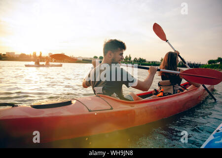 Certain young caucasian couple kayak sur rivière avec coucher du soleil dans l'arrière-plan. Avoir du plaisir dans l'activité de loisirs. Romantique et heureux homme et femme sur le kayak. Le sport, les relations concept. Banque D'Images