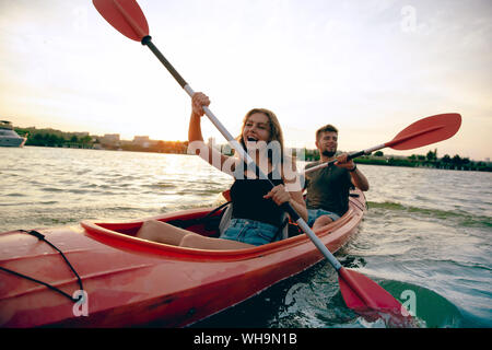 Certain young caucasian couple kayak sur rivière avec coucher du soleil dans l'arrière-plan. Avoir du plaisir dans l'activité de loisirs. Romantique et heureux homme et femme sur le kayak. Le sport, les relations concept. Banque D'Images