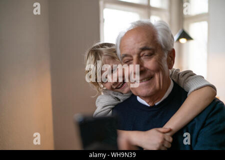 Petit-fils heureux grand-père serrant avec cell phone at home Banque D'Images