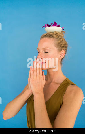 Femme blonde avec bol et pétales d'orchidée sur sa tête, sur fond bleu Banque D'Images