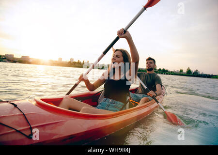 Certain young caucasian couple kayak sur rivière avec coucher du soleil dans l'arrière-plan. Avoir du plaisir dans l'activité de loisirs. Romantique et heureux homme et femme sur le kayak. Le sport, les relations concept. Banque D'Images