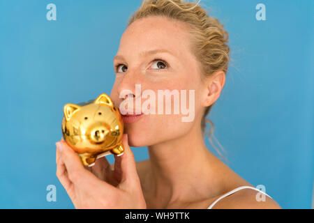 Portrait of blond woman kissing golden piggy bank Banque D'Images