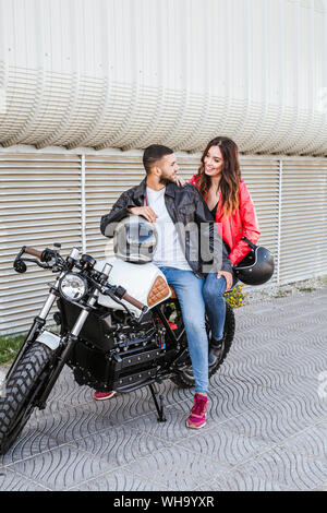 Couple heureux avec les casques de moto assis sur moto Banque D'Images