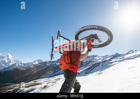 Les vététistes transporter leurs vélos d'une colline couverte de neige dans l'Himalaya au Népal avec vue sur les montagnes de Langtang, Népal, Asie Banque D'Images