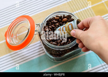 Mettre la main femme un rouleau d'une centaine de dollars dans un bocal en verre avec les grains de café sur une nappe. Pour les produits alimentaires en vrac peut comme cache ou coffre-fort. Banque D'Images
