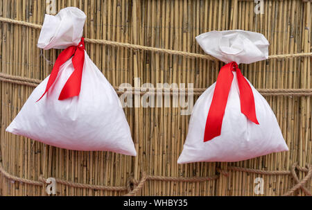 Deux sacs blancs avec des rubans rouges sur une clôture de bambou. Les sacs pour les cadeaux et surprises. Banque D'Images