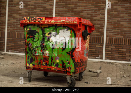 Le graffiti peint corbeille en face du mur de pierre très rouge avec de la peinture noire et jaune vert sur roues Banque D'Images