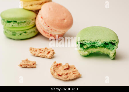 Un macaron vert à l'avant-plan se trouve une morsure.A proximité, miettes de la pâtisserie française. Dans l'arrière-plan, trois macarons colorés frais se trouvent dans une pile. Banque D'Images