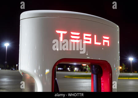 Haut du Superchargeur Tesla décrochage avec logo Tesla illuminé la nuit. Banque D'Images