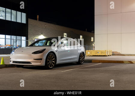 Tesla modèle 3 stationné à l'arrière d'une concession Tesla la la nuit. Banque D'Images