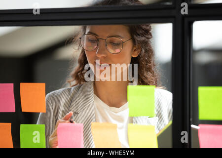 Young businesswoman écrire leurs idées sur des notes autocollantes sur conseil de verre Banque D'Images