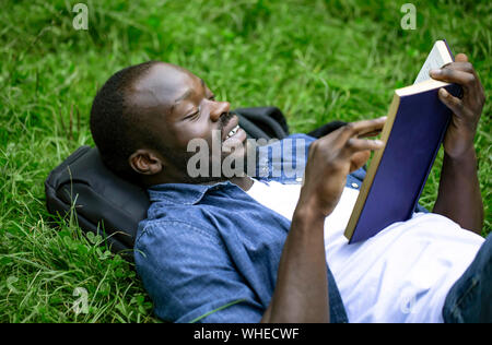 Joyeux africains-américains étudiant est emporté par la lecture allongé sur un campus park lawn Banque D'Images