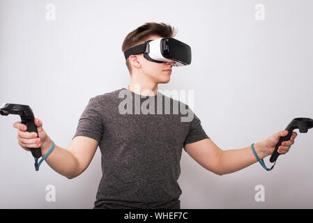 Jeune homme à lunettes viar. Un adolescent joue avec des lunettes de réalité virtuelle et considère les joysticks et gamepads. Banque D'Images