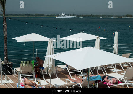 Parasols blancs et bleu ocean offrent un cadre idéal pour profiter d'un après-midi d'été sur l'île d'Ortigia, Syracuse, Sicile. Un yacht de luxe i Banque D'Images