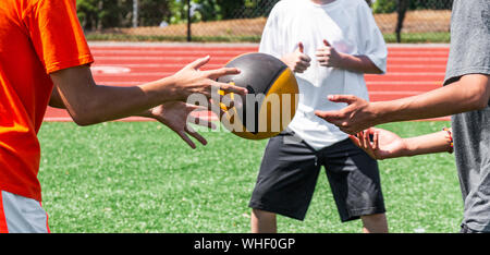 Trois adolescents sont de lancer un ballon sur le côté à l'autre pendant le force et agilité d'entraînement à la pratique sur le gazon vert. Banque D'Images