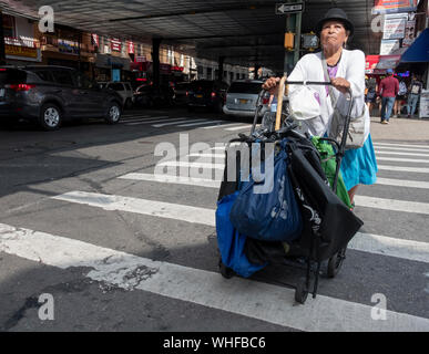 Une femme dans un chapeau, probaly cuisine mexicaine, traverse la rue en poussant un chariot. Sur l'avenue Roosevelt à Jackson Heights, Queens, New York. Banque D'Images