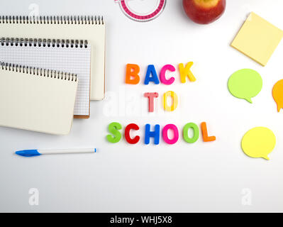 Inscription Retour à l'école de lettres en plastique de différentes couleurs et une pile de cahiers avec des draps blancs en blanc sur un fond blanc, vue du dessus Banque D'Images