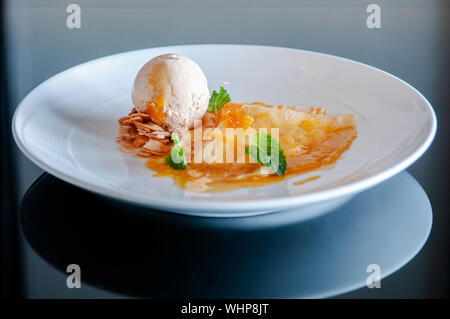 Crêpe française avec de l'orange douce au four sauce crème glacée à la vanille et amandes en plaque blanche sur le tableau noir Banque D'Images