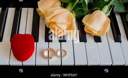 Comme un cadeau à la femme aimée, des roses jaunes se trouvent sur le piano avec bague de fiançailles et une boîte rouge en forme de cœur le jour du mariage, l'engagemen Banque D'Images