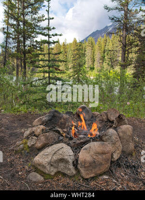 Brûler dans un feu de camp ring fait de grosses pierres sur le trajet d'une rivière de montagne dans la soirée. Banque D'Images