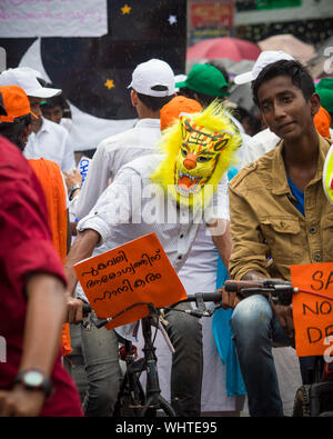 Kochi, Kerala State, India - 2 septembre 2019 - un garçon portant un masque de tigre randonnée à vélo avec des slogans écrits en malayalam au cours de Athachamayam Banque D'Images