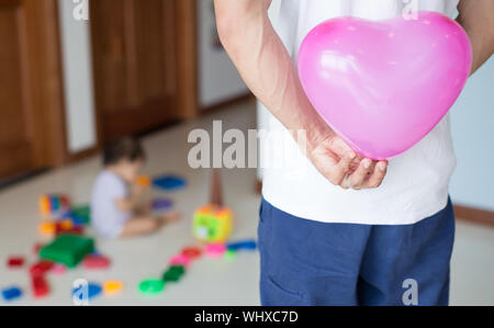 Père de cacher un ballon coeur rose derrière son dos, heureux de surprendre sa fille pour son anniversaire Banque D'Images