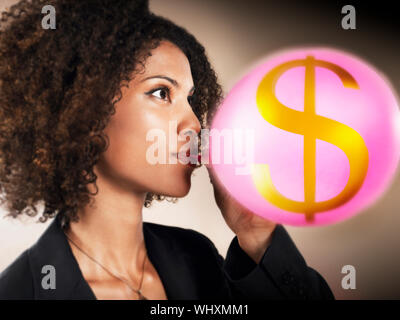 Closeup of a woman Blowing up balloon avec signe dollar contre fond brun Banque D'Images