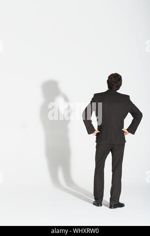 Vue arrière sur toute la longueur d'un homme avec les mains sur les hanches en faisant valoir son ombre contre fond blanc Banque D'Images