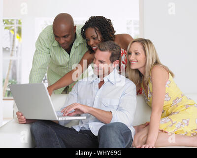 Quatre amis multiethnique sur canapé looking at laptop Banque D'Images