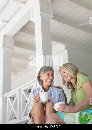 Deux femmes d'âge moyen heureux assis sur une véranda avec des tasses à café Banque D'Images
