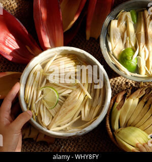 Vue de dessus les ingrédients pour préparer la nourriture végane de fleur de bananier, femme part prendre les jeunes les bananes, trempées dans de l'eau citronnée, de faire beaucoup de plats végétariens Banque D'Images