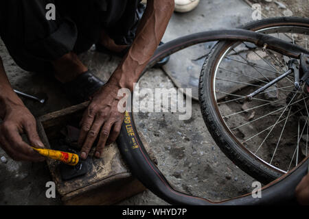 Un homme de réparation de vélos la fixation d'un pneu à plat sur un vélo sur une fin d'après-midi dans le nord de l'Inde. Banque D'Images