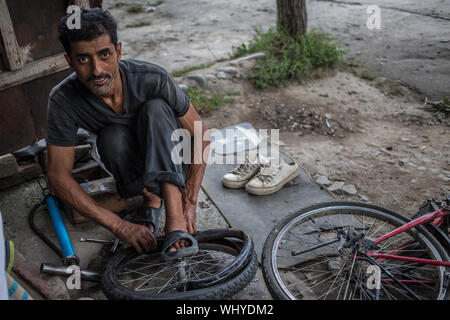 Un homme de réparation de vélos la fixation d'un pneu à plat sur un vélo sur une fin d'après-midi dans le nord de l'Inde. Banque D'Images