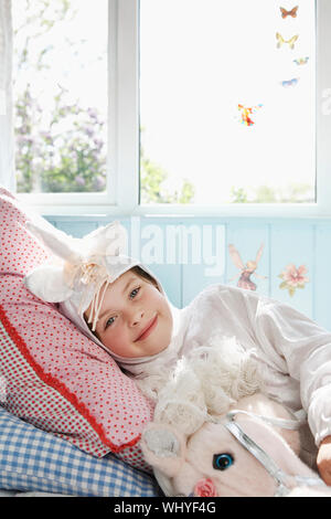 Portrait d'une jeune fille en costume de licorne au lit avec cheval jouet Banque D'Images