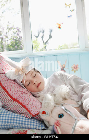 Jeune fille en costume de licorne sleeping in bed with toy horse Banque D'Images