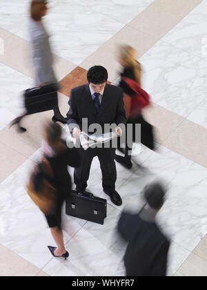Portrait of a businessman reading newspaper parmi les personnes floues marche sur sol carrelage Banque D'Images