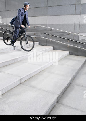 Vue latérale d'un businessman dans casque de vélo étapes vers le bas Banque D'Images