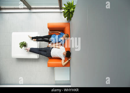 Vue de dessus deux personnes occasionnels vous coucher sur un canapé dans salon de réception à l'office de tourisme Banque D'Images