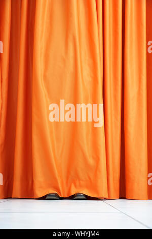 Avis de chaussures vu se cacher derrière le rideau orange Banque D'Images