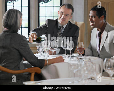 Trois businesspeople sitting at table de restaurant que l'homme verse le vin Banque D'Images