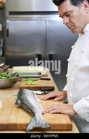 Vue latérale d'un homme d'âge moyen chef looking at salmon in kitchen Banque D'Images