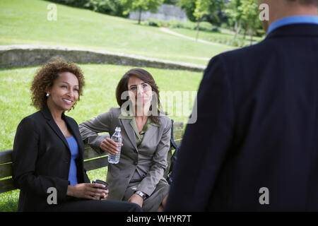 Deux femmes d'multiethnique sur banc de parc à la recherche d'affaires à Banque D'Images