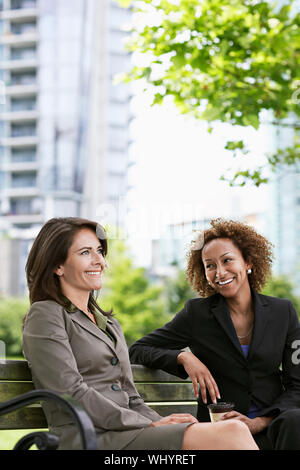 Deux smiling businesswomen sitting on park bench Banque D'Images