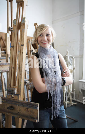 Smiling young female student standing au milieu de chevalets en art college Banque D'Images