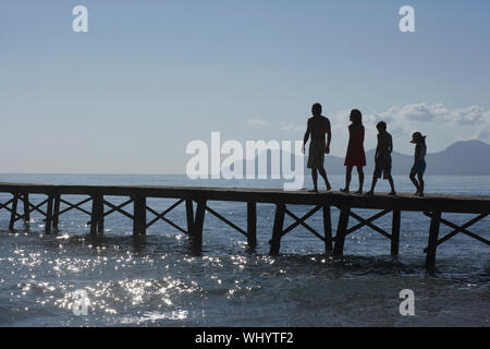 Toute la longueur de la silhouette les parents et deux enfants de marcher on jetty Banque D'Images