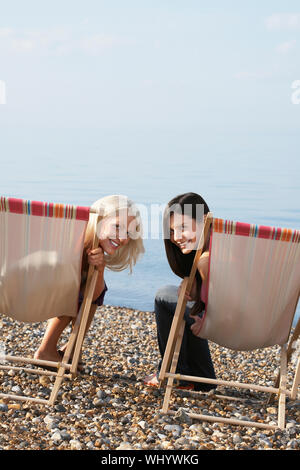 Portrait of happy female friends assis sur des chaises longues à la plage Banque D'Images