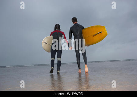 Vue arrière du couple avec planches à marcher en direction de la plage à la mer Banque D'Images