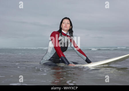 Belle femme surfer à l'écart tout en étant assis sur une planche de surf dans l'eau à la plage Banque D'Images